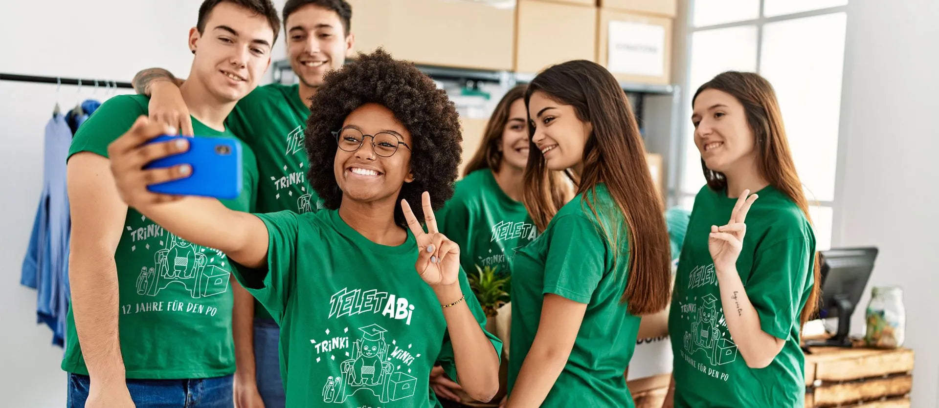 Abiturientengruppe in grünen T-Shirts mit Teletabi-Motiv-Druck beim Gruppen-Selfie